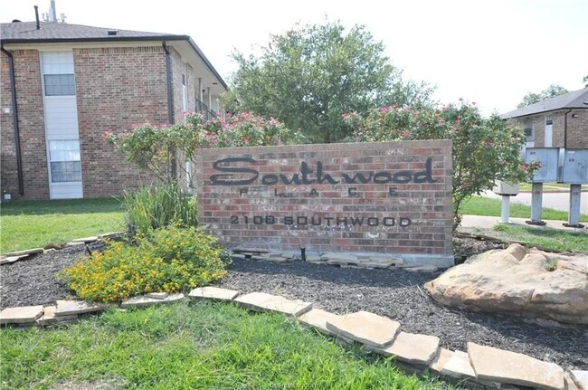 Brick sign reading "Southwood Village, 2108 Southwood" surrounded by landscaping and apartment buildings in the background.